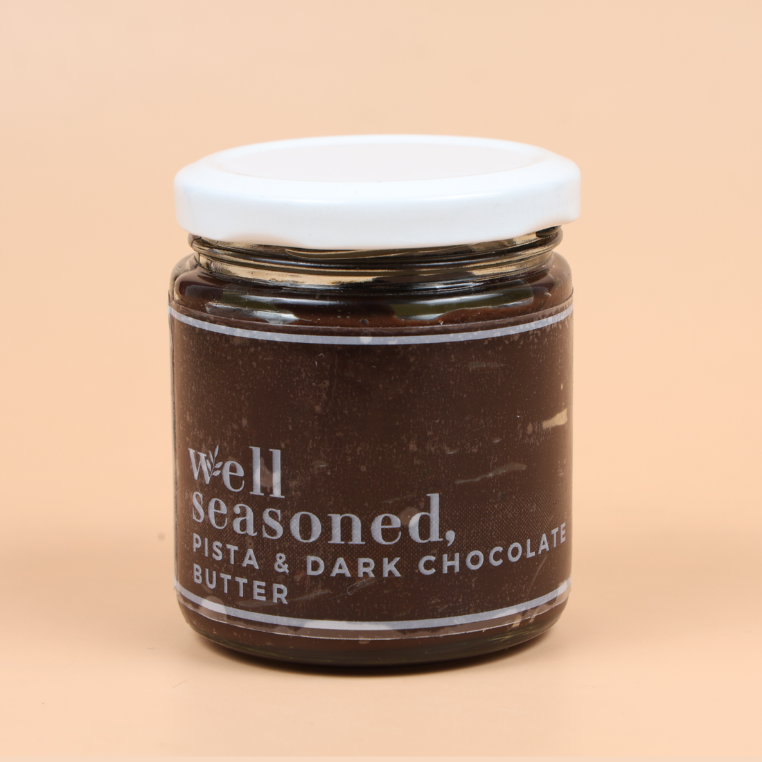 Person holding a jar of 'well seasoned' pistachio & dark chocolate butter with a spoon.