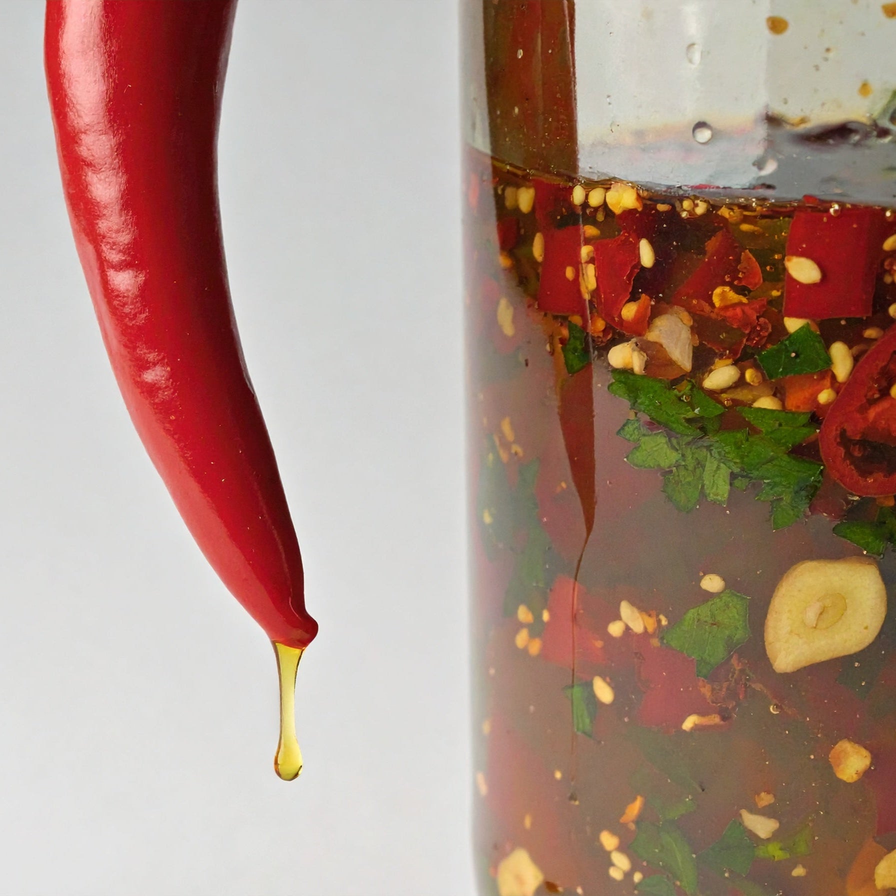 Glass bottle with a red chili pepper and various ingredients on a white background