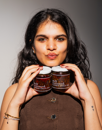 manika holding two jars of well seasoned, classic chili oil & korean chili oil 