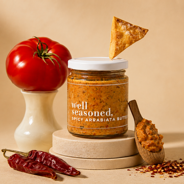 Jar of 'well seasoned' spice mix with a tomato, pepper, and tortilla chip on a beige background